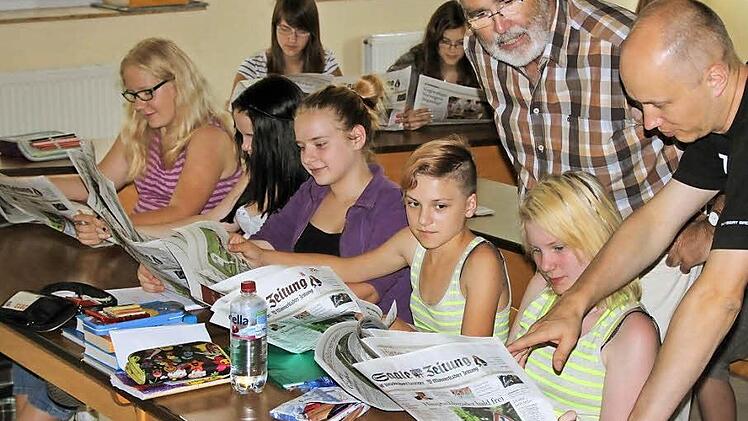 Lehrer Walter Kuhn (oben) und Redakteur Ralf Ruppert (rechts) besprechen mit den Schülerinnen (erste Reihe, von links) Judith Gran, Magdalena Zeier, Maria Allitaj, Pia Schlereth und Seline Rein den Aufbau der Saale-Zeitung. Hinten sind Aileen Resch und Ann-Kathrin Henkel zu sehen. Fotos: Ralf Ruppert / Sebastian Vogt