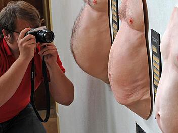 Ein Fotograf begutachtet Bierbäuche in einer Kunstausstellung.  Foto: Matthias Hiekel/dpa