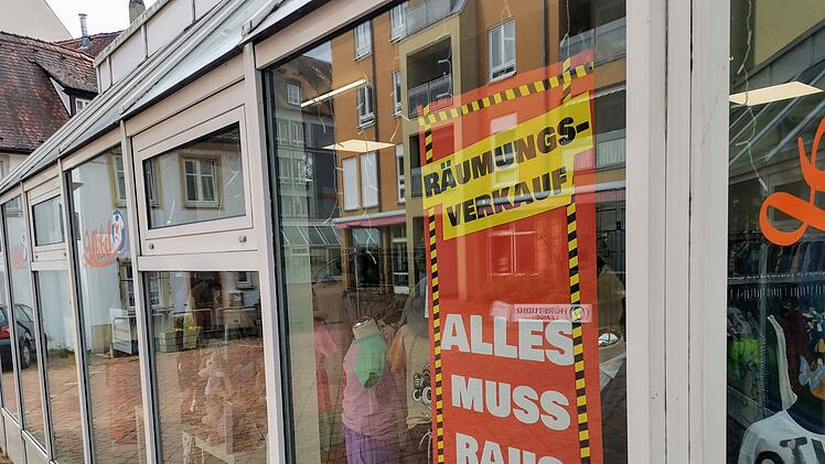 Ein Schaufenster mit buntem Schild &bdquo;R&auml;umungsverkauf&ldquo; und &bdquo;Alles muss raus&ldquo;. Innen sind Kinderkleidung und Schaufensterpuppen zu sehen.