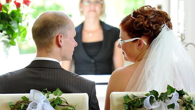 Ein junges Hochzeitspaar schaut sich w&auml;hrend seiner Trauung vor der Standesbeamtin an.  Foto: Patrick Pleul, dpa
