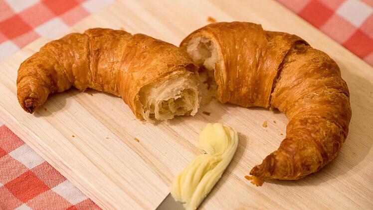 Ein Bamberger Hörnla, auf einem Brettchen liegend mit einem Messer mit Butter.