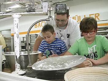 Bäcker Ulrich Müller zeigt Julian Pötzinger und Florian Zapf die richtigen Handgriffe. Mit der alten Waage wird die Brotmenge abgewogen. Denn ein "Ein-Pfund-Brot" muss auch wirklich ein Pfund wiegen. Foto: Adam