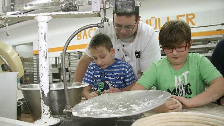 Bäcker Ulrich Müller zeigt Julian Pötzinger und Florian Zapf die richtigen Handgriffe. Mit der alten Waage wird die Brotmenge abgewogen. Denn ein "Ein-Pfund-Brot" muss auch wirklich ein Pfund wiegen. Foto: Adam