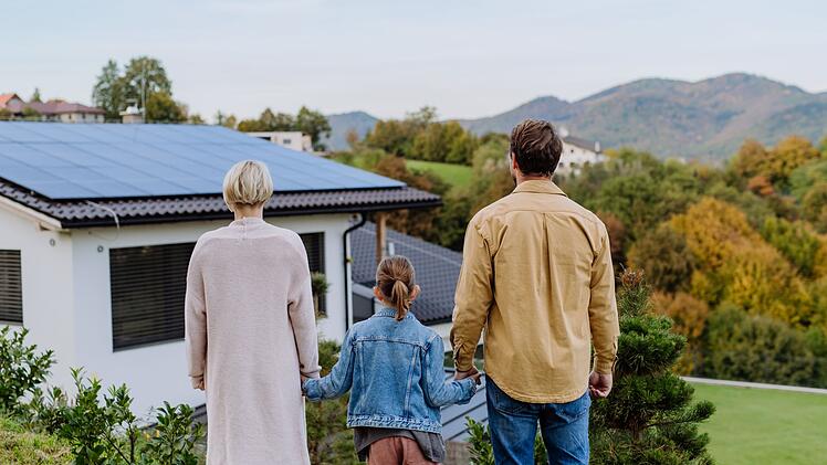 Rear view of family looking at their house with installed solar panels. Alternative energy, saving resources and sustainable lifestyle concept.