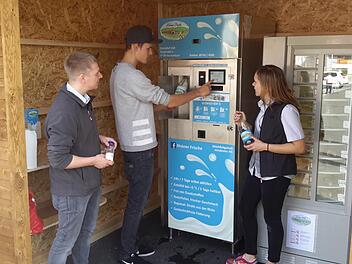 So einfach funktioniert es. Kevin Klüber (Bildmitte) erläutert Sebastian und Monika Hauke vom gleichnamigen Rewe-Markt die Bedienung der Milchtankstelle. Der neue Automat ist an sieben Tagen in der Woche rund um die Uhr in Betrieb.                       Foto: Rolf Pralle