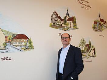 Dieter Muth steht im Konferenzzimmer des Rathauses der Gemeinde Oberleichtersbach. Die fünf Gemeindeteile sind an der Wand verewigt.  Foto: Julia Raab