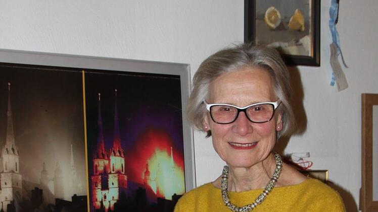 Adelheid Zimmermann sitzt vor einer Collage, die sie aus Fotografien ihres Vaters angefertigt hat. Sie zeigen dessen Heimatstadt Halle. Foto: Ulrike Müller