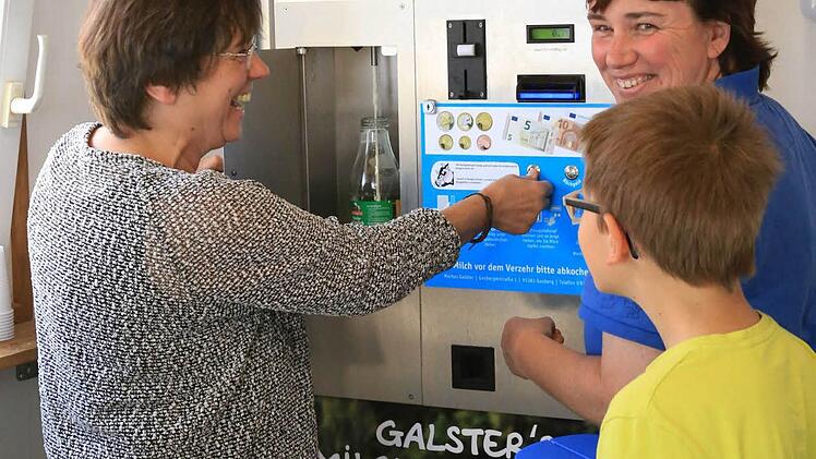 Helga Deinhardt holt sich ihre erste Flasche Milch aus dem Automaten, rechts Christine Galster und Elias, der den Tankvorgang interessiert beobachtet.  Fotos: Franz Galster