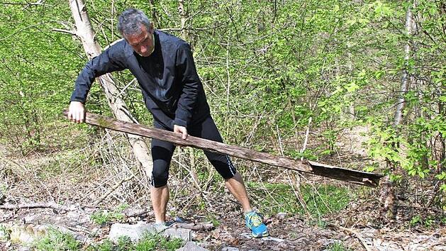 Hubert Karl zeigt, was &uuml;brig ist vom Zeiler Trimm-Dich-Pfad: Das halb verrottete Schild, das die Station 15 (Fu&szlig;-Erlebnis-Pfad) beschreibt, hat er aus dem Gestr&uuml;pp hervorgezogen. Aber gelogen ist es ja nicht, was da drauf steht: Es ist immer noch ein Fu&szlig;-Erlebnis, wenn man &uuml;ber die Reste der Station hinweg l&auml;uft. Fotos: Andreas L&ouml;sch