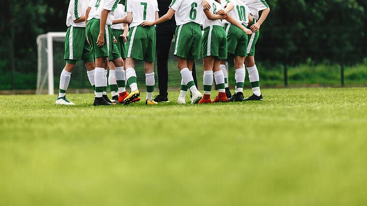 Glückliche Fußballmannschaft. Motivierte Jugendfußballmannschaft jubelt auf dem Spielfeld. Trainer spricht mit einer Gruppe von Fußballspielern. Players huddling in a circle on the field. Happy football team. Motivated youth soccer team cheering on court. Coach talking to a group of soccer players.