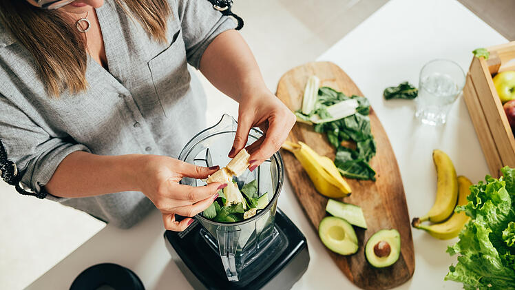 Woman is preparing a healthy detox drink in a blender - a  green