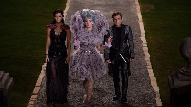 Katniss (Jennifer Lawrence, links) und Peeta (Josh Hutcherson) m&uuml;ssen noch einmal zu den t&ouml;dlichen Spielen in der Arena von Panem antreten. Anstandsdame Effie Trinket (Elizabeth Banks) versucht, die beiden f&uuml;r einen Empfang zum L&auml;cheln zu animieren.