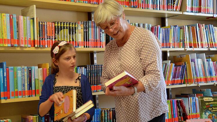 Amelie Götz hat die meisten Bücher im Regal hinter ihr schon gelesen. Deshalb sucht sie mit der Leiterin der Katholischen Öffentlichen Bücherei, Elisabeth Kuhn, nach einem neuem Lesestoff.  Foto: Kathrin Kupka-Hahn