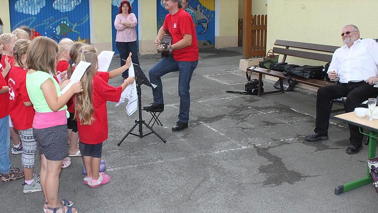 Die Roth-Kehlchen mit Chorleiter Stefan Kriegel singen im Schulhof für Schulleiter Michael Barnickel (r.) der im Stuhl sitzt und den Gesang genießt. Foto: Gerd Klemenz