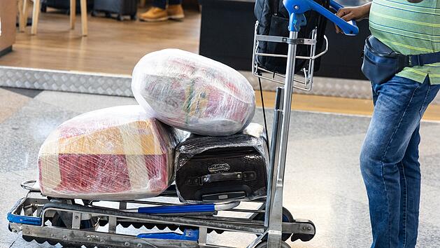 Reisender am Flughafen mit Gep&auml;ck auf einem Trolley, der aus Sicherheitsgr&uuml;nden mit Schutzfolie umwickelt ist. Traveler at airport with luggages on trolley wrapped with protective film for safety