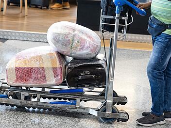 Reisender am Flughafen mit Gepäck auf einem Trolley, der aus Sicherheitsgründen mit Schutzfolie umwickelt ist. Traveler at airport with luggages on trolley wrapped with protective film for safety