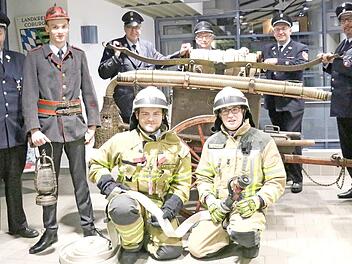 Die alte Pompino-Feuerspritze, Uniformen, Anzüge und Ausrüstungsgegenstände aus verschiedenen Zeiten präsentieren (von links): Kommandant Bernd Lemser, Jonas Götz, Ulrich Gräbner, Uwe Lambrecht, Thorsten Langbein, Vorsitzender Ralf Wagner und Matthias Lemser sowie (vorne kniend, von links) Max Reisenweber und Kai Schwegler.  Foto: Alexandra Kemnitzer