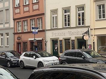 Stra&szlig;enszene in Bamberg: Mehrere Autos parken vor Altbauten in der Innenstadt. Eine Bar mit Schild ist zu sehen; ein neues Konzept wird den Standort beleben.
