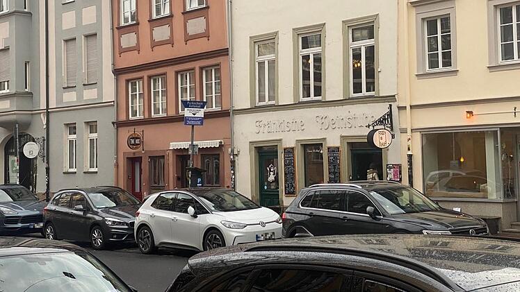 Stra&szlig;enszene in Bamberg: Mehrere Autos parken vor Altbauten in der Innenstadt. Eine Bar mit Schild ist zu sehen; ein neues Konzept wird den Standort beleben.