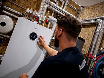 Handwerker zeigt an einer W&auml;rmepumpe auf die Anzeige