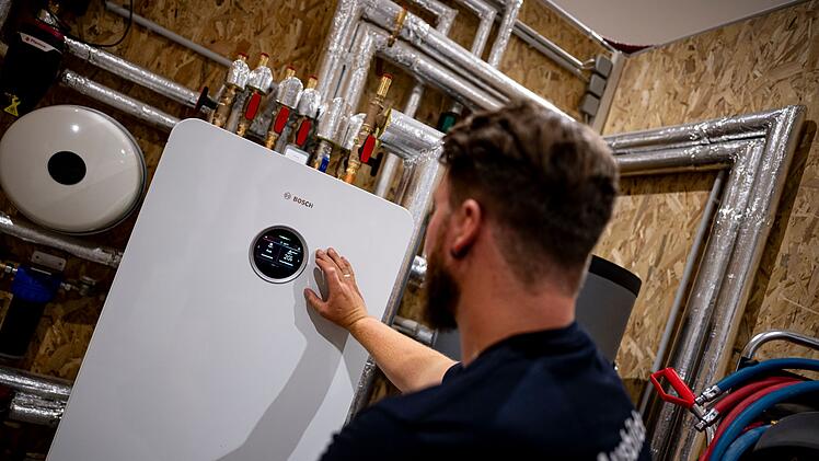 Handwerker zeigt an einer W&auml;rmepumpe auf die Anzeige