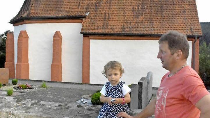 Die zweijährige Lenia war die jüngste Teilnehmerin bei der Ortsbegehung in Birkach. Ihr Papa, Manfred Schirdewahn (rechts), war damit als Gemeinderat, Bauhofleiter der Gemeinde Burgpreppach und Kindermädchen gleich in dreifacher Funktion gefordert. Im Hintergrund die Friedhofskapelle.  Foto: Gerhard Schmidt