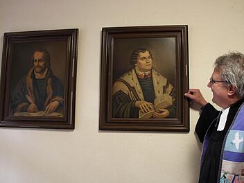 Blickt zu den Reformatoren auf: Pfarrer Gerd Kirchner kennt die Bedeutung der Reformatoren Philipp Melanchthon (links) und Martin Luther für die Entstehung der evangelischen Kirche. Die Bilder hängen in der Sakristei der Christuskirche im Staatsbad Bad Brückenau. Foto: Ulrike Müller