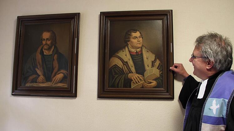 Blickt zu den Reformatoren auf: Pfarrer Gerd Kirchner kennt die Bedeutung der Reformatoren Philipp Melanchthon (links) und Martin Luther für die Entstehung der evangelischen Kirche. Die Bilder hängen in der Sakristei der Christuskirche im Staatsbad Bad Brückenau. Foto: Ulrike Müller