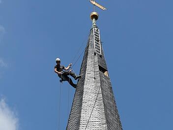 Ein Mitarbeiter des "Team Alpin" inspiziert in schwindelerregender Höhe die Schieferziegeln an der Außenwand des Kirchturms. Foto: Christian Dreßel