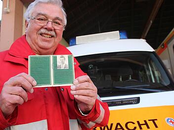 Hans Thunig zeigt den Pass von 1959, der bestätigt, dass er mit 15 Jahren den sogenannten Grundschein abgelegt hat. Im Hintergrund ist das Einsatzfahrzeug der Wasserwacht zu sehen. Foto: Heike Beudert
