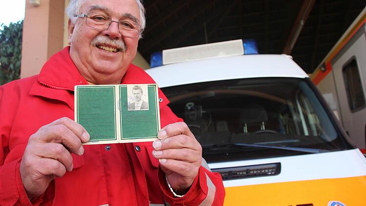 Hans Thunig zeigt den Pass von 1959, der bestätigt, dass er mit 15 Jahren den sogenannten Grundschein abgelegt hat. Im Hintergrund ist das Einsatzfahrzeug der Wasserwacht zu sehen. Foto: Heike Beudert