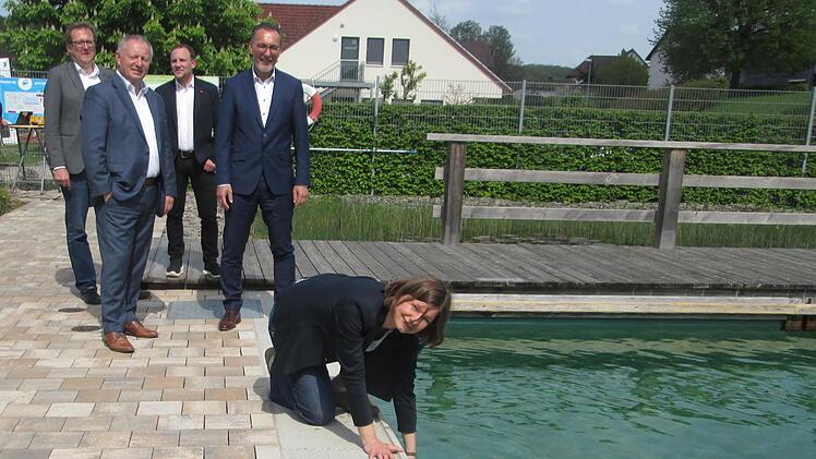 Wie ist das Wasser? "Angenehm erfrischend", meinte die Bundespolitikerin Manuela Rottmann, die das Natur-Freibad Aura mit Anerkennung bedachte. Zuschauer beim "Wassertest" sind DVS-Moderatoren Moritz Kirchesch und Stefan Kämper sowie Landrat Thomas Bold und Bürgermeister Thomas Hack.