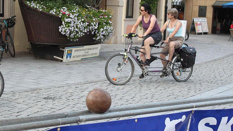 An der Kegelbahn: Rad fahrende Passanten ohne Blick für den Rücklauf einer Kegelkugel.