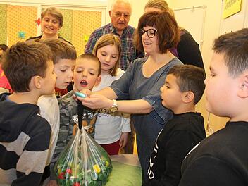 Tina Lauer wiegt das Säckchen mit den Plastikdeckeln ab und lässt die Kinder das Gewicht raten. Im Hintergrund verfolgen Helene Sabelfeld und Hendrik Seegebarth die Aktion.  Fotos: Bernhard Panzer