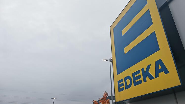 Ein gro&szlig;es EDEKA-Logo prangt an einem Geb&auml;ude. Der Himmel ist bew&ouml;lkt; im Vordergrund sind Herbstb&auml;ume zu sehen. Ein Bamberger EDEKA-Markt hat Ma&szlig;nahmen wegen Diebstahl getroffen.