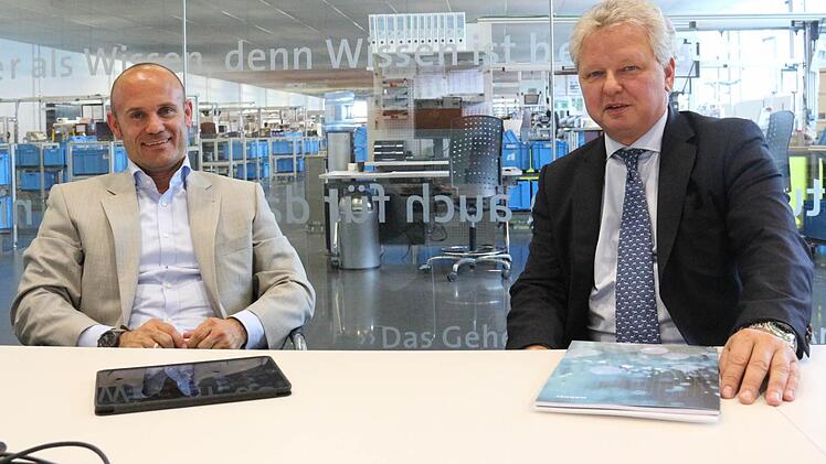 Björn Schumacher und Frank Wöhner im Besprechungszimmer mit Durchblick in die Fertigung bei Wöhner. Beide Unternehmer sind überzeugt davon, dass ihre Unternehmen sich nur dann weiterentwickeln können, wenn es möglich ist, von Coburg aus zu den übrigen Standorten zu fliegen.Foto: Simone Bastian