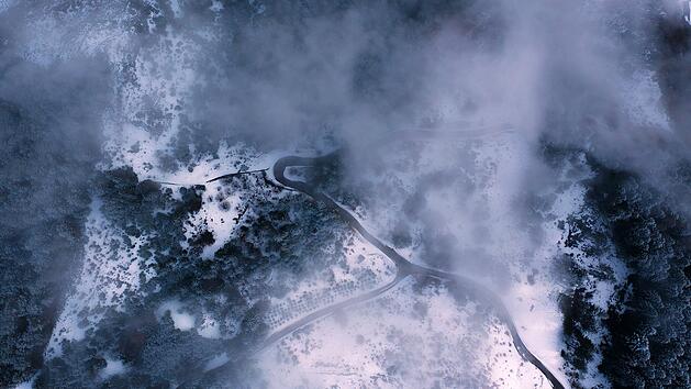 Luftaufnahme einer tags&uuml;ber nebelverhangenen Bergstra&szlig;e im Zillertal, Tirol, &Ouml;sterreich. An aerial view of mountain road covered with fog during daytime in Zillertal, Tyrol, Austria.Cartelbishop/Wirestock Creators