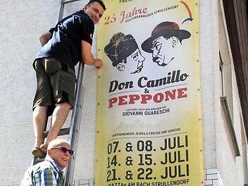 Bläcky Schwarzmann (unten) und Stefan Wagner befestigen in der Bamberger Straße, nur einen Steinwurf von der "Piazza" entfernt, ein Längs-Banner für das Jubiläums-Freilichttheater. Foto: Bertram Wagner