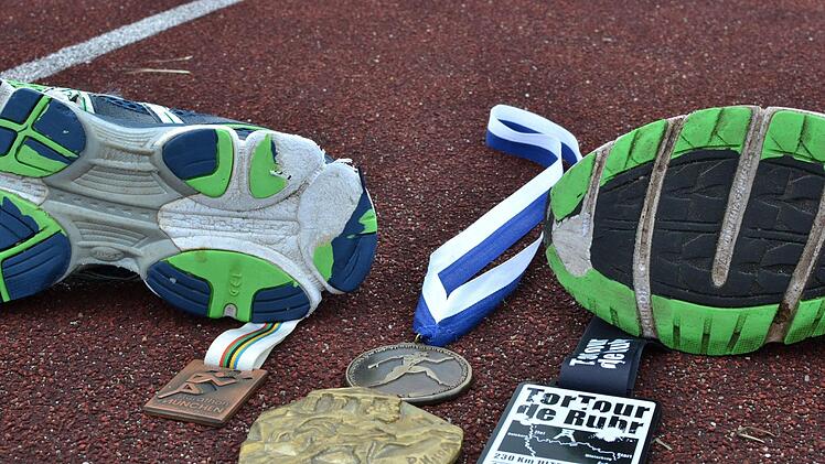 Die Medaillen seines ersten Marathons in München 1984, die des Sparthathlons und die des Ultralaufs TorTour de Ruhr. Im Hintergrund sind Karls deutlich abgewetzte Laufschuhe zu sehen.