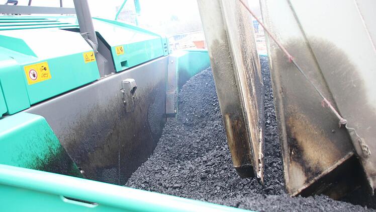 Der heiße Asphalt ergießt sich aus dem Laster in die Asphaltmaschine. Foto: Friedwald Schedel