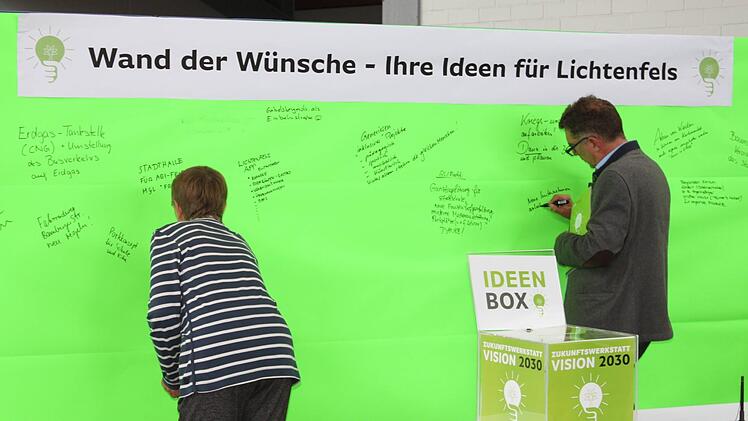 Auf leuchtendem Grün bringen zwei Besucher Anregungen an.