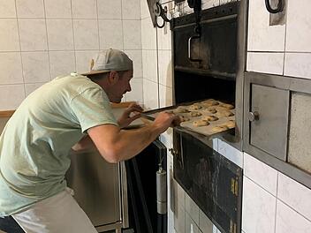 Steffen Schneider schiebt ein Bleck mit Backwaren in den Ofen des Dorfbackhauses. Das Haus ist dank ehrenamtlichem Engagement der Dorfbewohner neu gestaltet. Foto: Thomas Malz