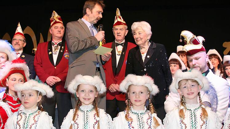 Umrahmt von den Gardetänzerinnen des Vereins hielt Dritter Bürgermeister Michael Rädlein (mit Mikrophon) eine Laudatio auf 33 Jahre Karnevalsvereins Weidach, zu deren Erfolg die "Grande Dame des Weidacher Karnevals", die 92-jährige Lieselotte Engemann (rechts) beigetragen hat. Dahinter (von links): Landrat Michael Busch, 1. Vorsitzender Michael Forkel, "Urgestein" Günter Forkel sowie (knieend) Sitzungspräsident Christian Brettschneider. Foto: Bettina Knauth