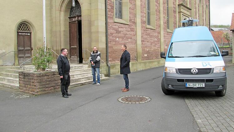 Pfarrer Norbert Wahler, Bauhofangestellter Christian Reusch und Bürgermeister Johannes Krumm (von links) lauschen neben dem BR-Aufnahmefahrzeug dem Zwölf-Uhr-Läuten.