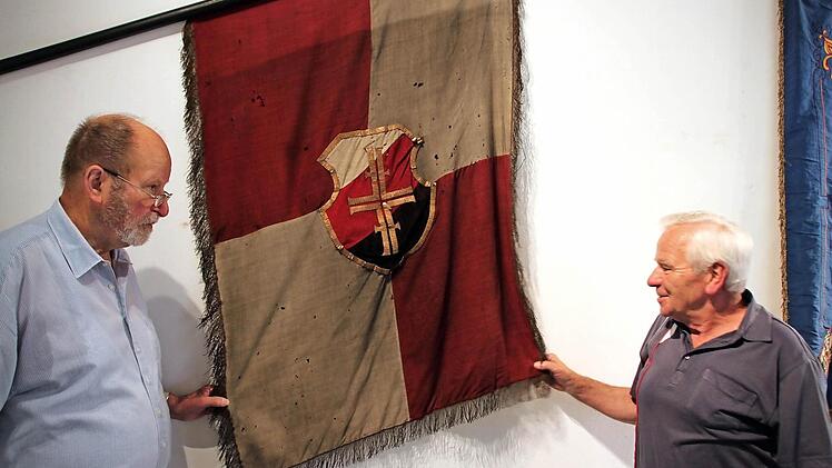 Walter Andres (rechts) und Karl Beudert (links) betrachten das älteste Ausstellungsstück, die Gründungsfahne aus dem Jahr 1863.