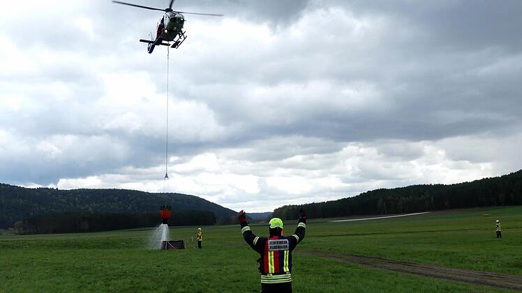Ein Flughelfer weist den Hubschrauber ein, der versucht, den Wassercontainer am Boden zu befüllen