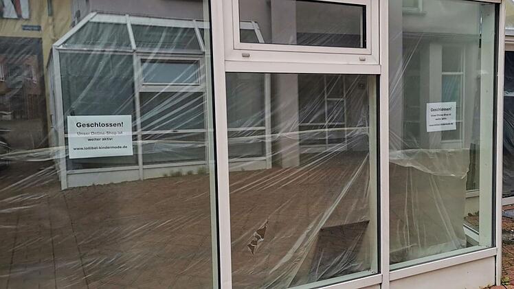 Ein Ladengesch&auml;ft mit Schaufenstern, teils verh&uuml;llt, zeigt ein "Geschlossen"-Schild. Online-Shop bleibt aktiv, w&auml;hrend neuer Mieter erwartet wird.