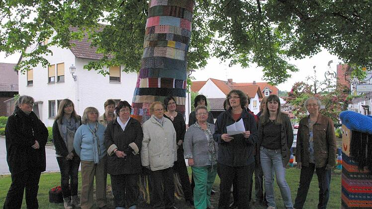 Im Schatten der Dorflinde präsentiert sich Gemünda im neuen Gewand. "Wir sind die Guerilla-Gruppe der Kirchengemeinde", scherzte Pfarrerin Kathrin Neeb (links) bei der Präsentation des bestrickten Dorfplatzes am Sonntag. Diese Art der Straßenkunst wird als Urban oder Guerilla Knitting bezeichnet. Rund 15 Frauen der Gemünner Lichtstube unter Leitung von Barbara Hämmelmann (im Vordergrund) haben das Projekt auf die Beine gestellt. Foto: Bettina Knauth