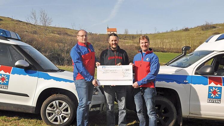 Michael Hahn von den Clubfreunden aus Burk (M.) &uuml;bergibt am Walberla-Plateau den symbolischen Scheck an die Bergwachtler Thomas Obeth und Daniel Lochner (r.). Foto: Leo H&uuml;hnlein