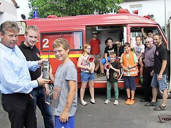 Kommandant Christopher Stübinger und der Vorsitzende Torsten Grampp erklären Lukas Leitner (12), wie man ein Funkgerät richtig benutzt. Im Hintergrund erkunden die anderen Feuerwehrkinder das Auto: Larissa Grampp (11), Leon Wienoreck (10), Moritz Schatz (9), Johannes Michel(12), Jonas Ostbonk (8), Fabio Täuber (11), Jasper Hain (9) sowie Jakob Michel (10) mit Stadtrat Lothar Seyfferth und dem stellvertretenden Kommandanten Heiko Hofmann, der die neue Kindergruppe leitet.  Foto: Sonja Adam